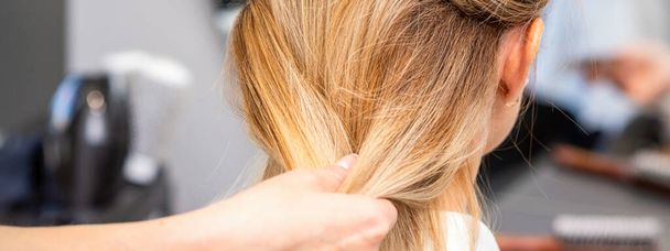 Gros plan des mains de coiffeuse coiffant les cheveux d'une femme blonde dans un salon de coiffure - Photo, image