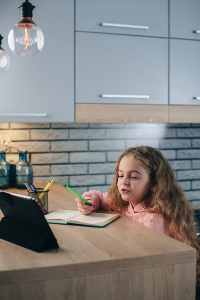 Blonde lovely girl is using a tablet during online lessons in the kitchen from home - Φωτογραφία, εικόνα