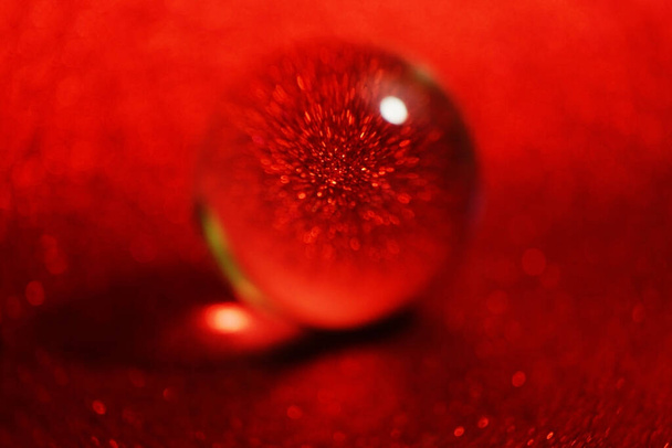 Niesamowite i piękne makro kryształowej kuli na czerwonym brokatowym tle purpurynowym, które wygląda jak kropla wody - Zdjęcie, obraz