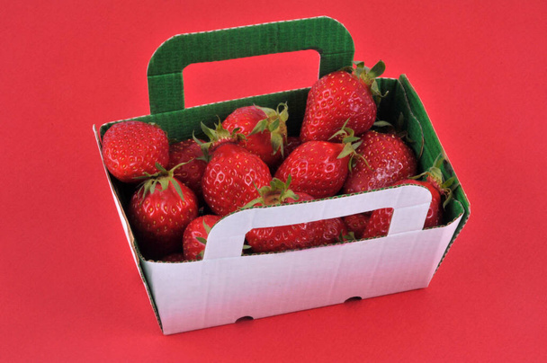 Punnet de cartón de gariguetas fresas primer plano sobre fondo rojo - Foto, imagen