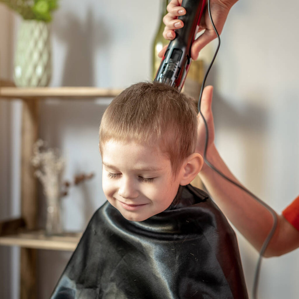 A young woman in bright clothes is cutting a little boy's hair using hair clipper. Concept of family, care, lifestyle. - Фото, зображення