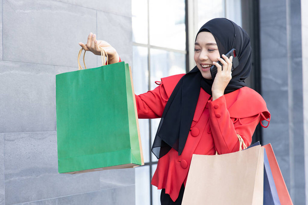 Σύγχρονος τρόπος ζωής της αραβικής μουσουλμάνων νεαρή γυναίκα σε πέπλο μαντίλα με τσάντες ψώνια με τα πόδια για ψώνια τηλέφωνο δρόμο καλώντας. - Φωτογραφία, εικόνα
