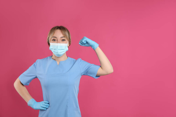 Doctor with protective mask showing muscles on pink background, space for text. Strong immunity concept - Foto, imagen