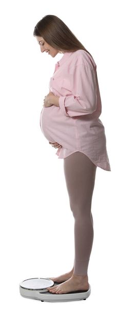 Pregnant woman standing on scales against white background - Foto, Imagem