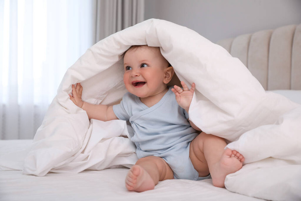 Cute little baby under soft blanket on bed at home - Zdjęcie, obraz