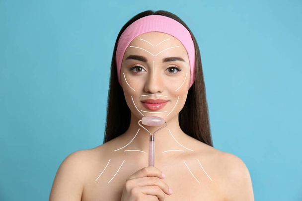 Woman using natural face pink quartz roller on light blue background - Foto, immagini