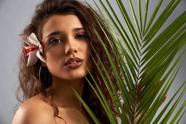 Woman with orchid behind ear holding palm leaf. - Foto, immagini