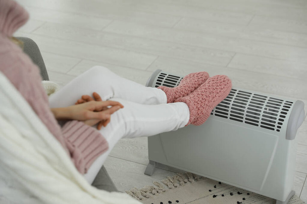 Woman warming feet on electric heater at home, closeup - Photo, image