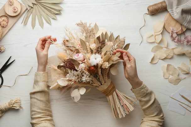 Florist making beautiful bouquet of dried flowers at white table, top view - 写真・画像