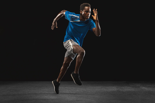 Young African-American man, athlete training isolated over black background. - Zdjęcie, obraz