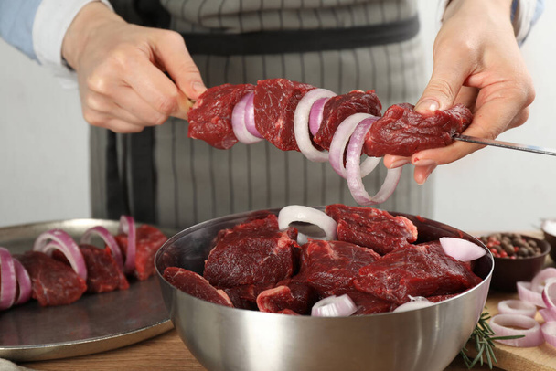 Woman stringing marinated meat on skewer at wooden table, closeup - Foto, immagini