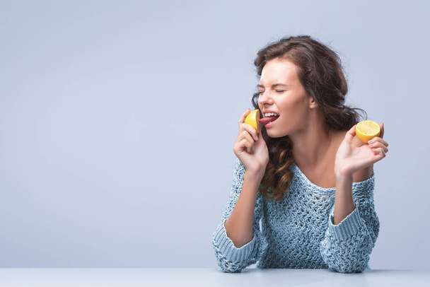 Cute brunette woman holding two halves of yellow lemon citrus fruit in hands and biting wth appetite first half - Fotó, kép