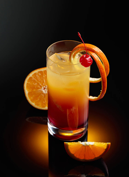 Koktél tequila napkelte cseresznye és narancs szelet fekete fényvisszaverő háttér. - Fotó, kép