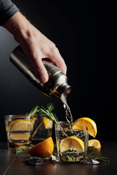 Cocktail Gin y Tonic con limón y romero. El camarero vierte un cóctel de una coctelera en un vaso. - Foto, Imagen