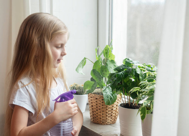 Kleines Mädchen, das Wasser auf Zimmerpflanzen spritzt. Gartenarbeit zu Hause - Foto, Bild
