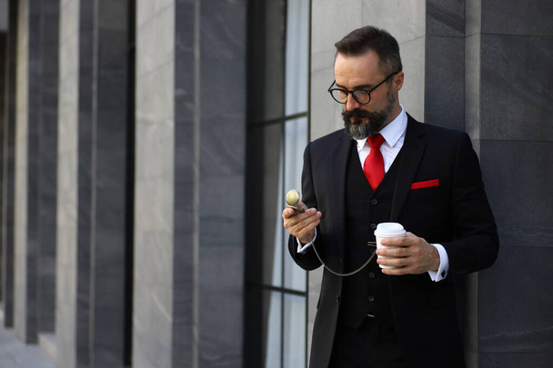 Kavkazský obchodník drží odnést šálek kávy sledování jeho staré módní kapesní hodinky mimo byt v dopoledních hodinách před odchodem do práce - Fotografie, Obrázek