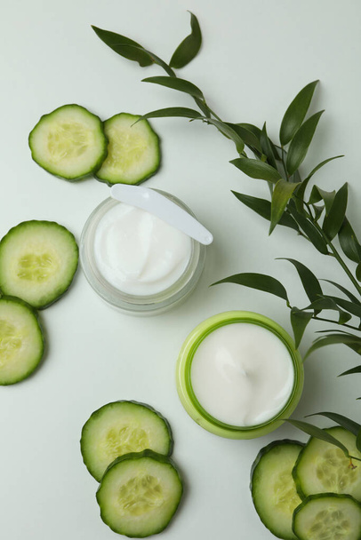 Jars with cosmetic cream, cucumber slices and branch on white table - Foto, Imagem