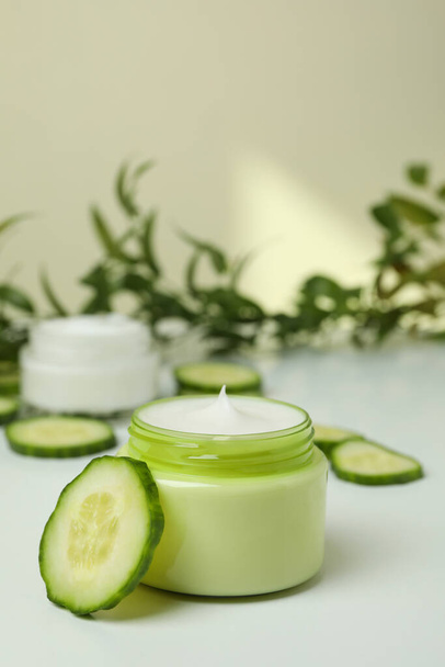 Jars with cosmetic cream, cucumber slices and branch on white table - Photo, Image