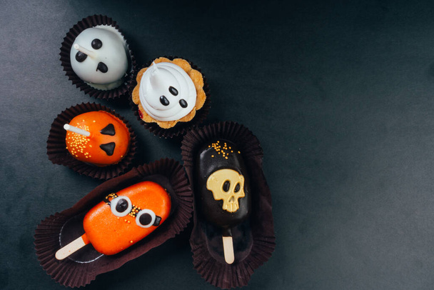 Halloween snoepjes en traktaties op zwarte achtergrond met kopieerruimte. Geest, schedel en monster symbool op party desserts - Foto, afbeelding