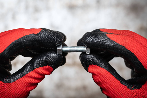 Osoba nosząca rękawice ochronne przytrzymujące śrubę i nakrętkę na metalowym tle - Zdjęcie, obraz