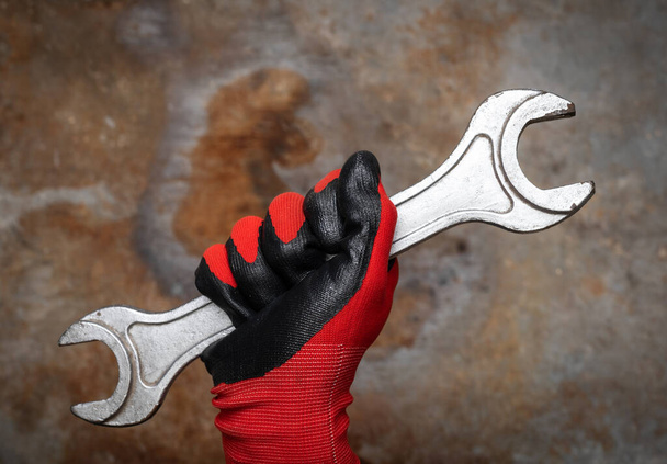 Person wearing protective glove holding big wrench against rusty metal background - Photo, Image