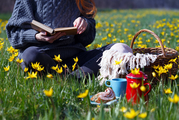 spring picnic in the meadow. girl  reads a book on the background beautiful wild yellow tulips.  still lif - Foto, imagen