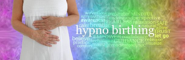 Hypnobirthing Word Cloudの利点-虹色の知恵のパターンの背景にHYPNOBirthingワードクラウドの横に胃全体の手を持つ白いドレスの女性  - 写真・画像
