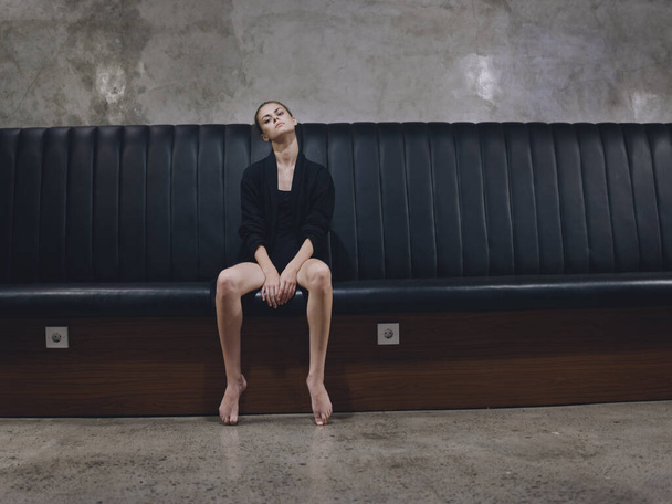 mujer descalza sentada en un banco modelo interior en ropa oscura - Foto, imagen