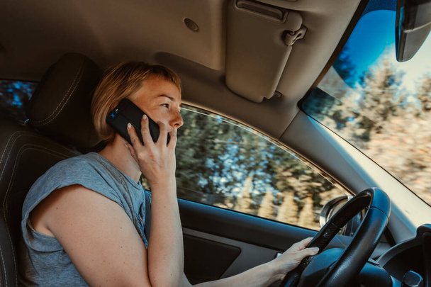 Genç bir kadın araba kullanırken cep telefonu kullanıyor. - Fotoğraf, Görsel