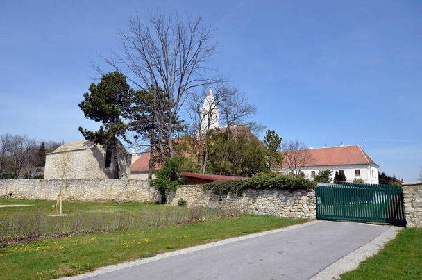 Österreich, die Pfarrkirche Margarethen am Moos ist umgeben von einem romanischen Beinhaus aus dem Jahr 1233, einem ehemaligen Kloster - heute Pfarrhaus und einer alten Steinmauer. - Foto, Bild
