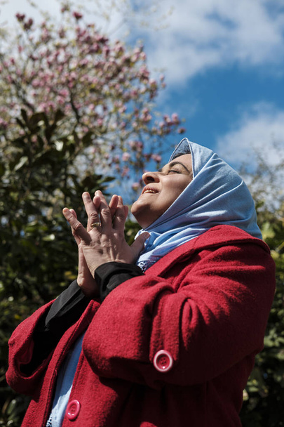 Зрелая мусульманка, носящая хиджаб, смотрит на солнце и молится. Прекрасное утро. - Фото, изображение