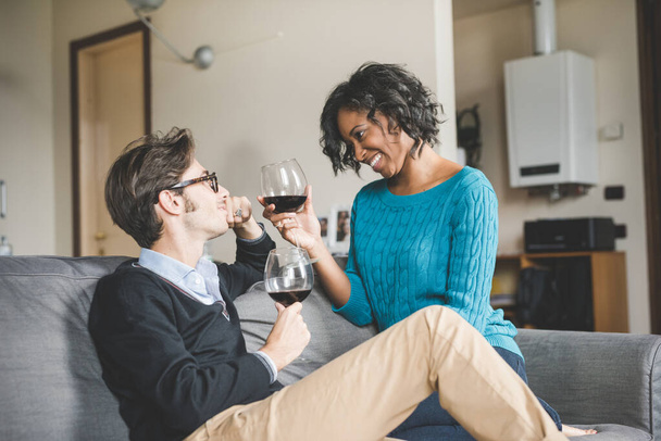Мультинациональная счастливая пара в любви празднует пить вино в помещении дома - Фото, изображение