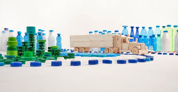 Drewniana ciężarówka jedzie ulicą w mieście plastikowych butelek i plastikowych nakrętek. Plastikowe miasto. Koncepcja wolna od tworzyw sztucznych. - Zdjęcie, obraz
