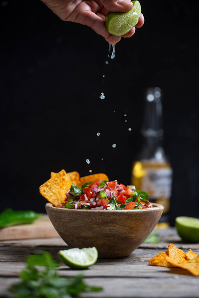 Man squeezes lime juice into a plate of homemade salsa pico de gallo, mexican cuisine - Foto, Imagen