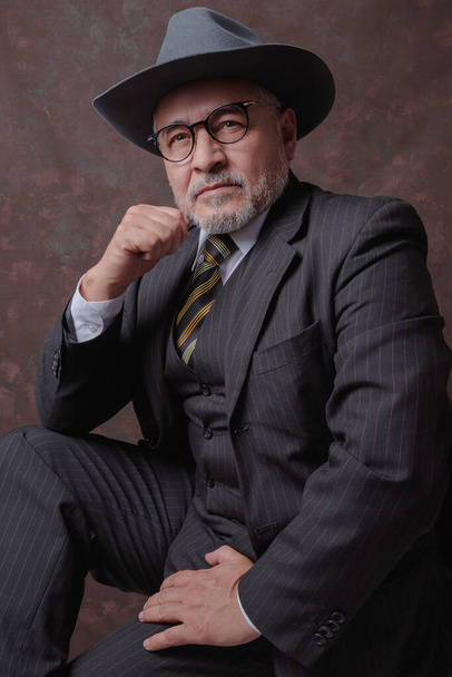 Een volwassen heer poserend voor de camera in een donkerbruin pinstripe pak en hoed - Foto, afbeelding