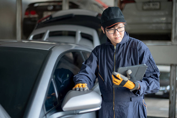 Asian auto mechanic holding digital tablet checking car wing mirror. Mechanical maintenance engineer working in automotive industry. Automobile servicing and repair concept - Photo, image