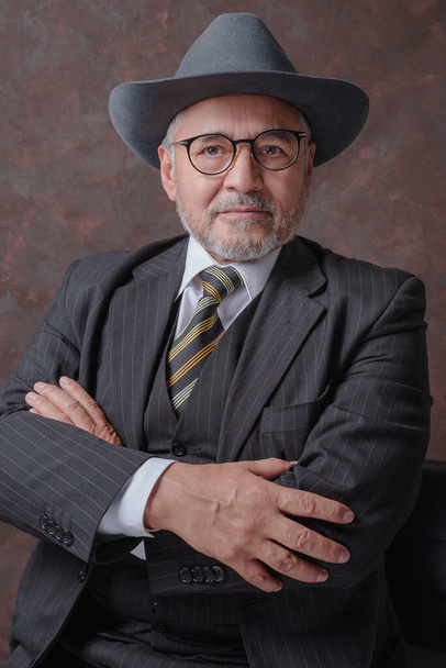 A mature gentleman posing for the camera in a dark brown pinstripe suit and hat - Foto, Imagen