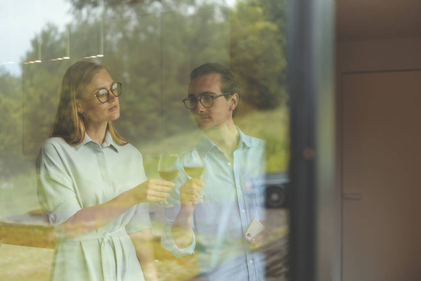 Portrait through a glass window of successful couple celebrating on the kitchen - Photo, Image