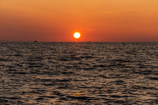 Un hermoso amanecer naranja está en la playa junto al mar con siluetas de barco negro - Foto, imagen