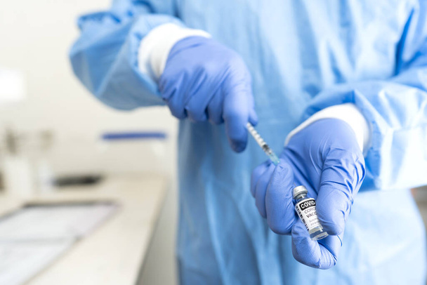 Konzept der globalen Impfung zur Bekämpfung der Covid-19-Pandemie: medizinisches oder medizinisches Personal im Vollschutzkoffer mit blauen Handschuhen bei der Vorbereitung einer Medikamenteninjektion zur Erstellung der Impfstoffdosis aus Fläschchen mit Spritze - Foto, Bild