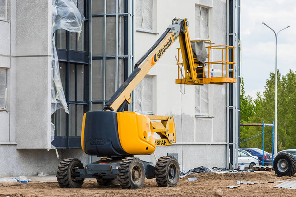 Białoruś, Mińsk - 28 maja 2020: Pojazd przemysłowy z platformą podnoszącą na tle nowego nowoczesnego budynku w budowie na placu budowy. - Zdjęcie, obraz
