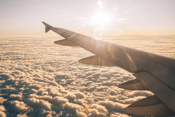 Die Sonne scheint hell auf die Wolken unter den Tragflächen des Flugzeugs. Blick aus dem Bullauge - Foto, Bild