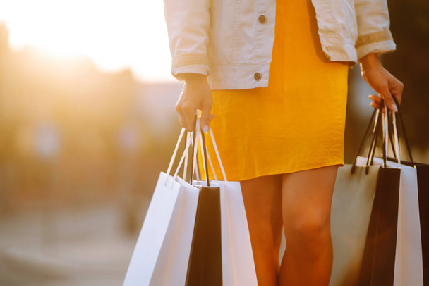 Shopping bags in the woman hands. Young woman with shopping bags walking on street. Spring shoopping. Consumerism, sale, purchases, shopping, lifestyle concept. - 写真・画像