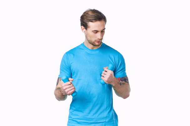 man met halters in een blauw t-shirt op een lichte achtergrond kijken naar de zijkant bijgesneden uitzicht - Foto, afbeelding