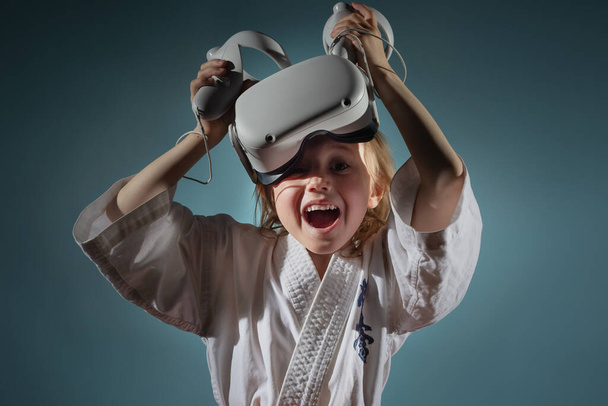 Studio Portrait of young caucasian girl in karate uniform playing video games with virtual reality headset or practicing online, embroidered text on kimono kyokushinkai. Banner. - Фото, изображение