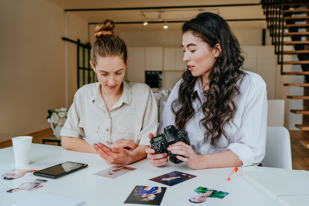 Two young women selecting photos on the camera indoor. Selective focus. - Foto, Bild