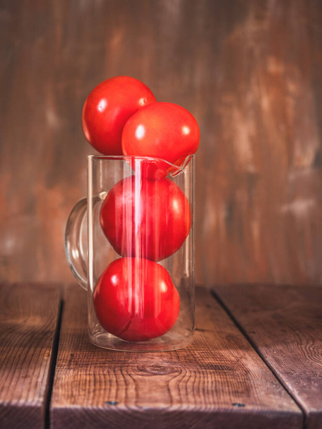 Glazen kan met rode tomaten op een bruine tafel verticaal frame close-up - Foto, afbeelding
