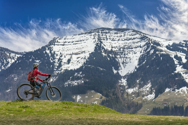 досить середнього віку жінка їде на електричному гірському велосипеді ранньою весною в горах Альгау поблизу Оберстауфена, під ефектним сніговим покриттям Гохретнаґельфлюхського ланцюга. - Фото, зображення