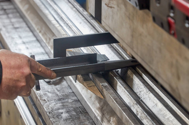 работник, держащий металлическую деталь на станке для гибки листа - Фото, изображение