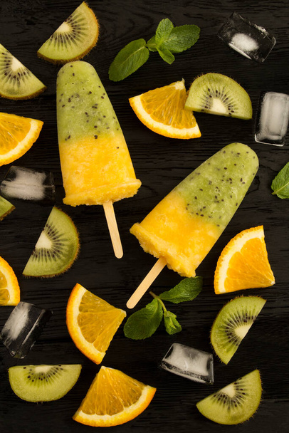 Top view of popsicles with kiwi and orange fruit on the black wooden  background. Close-up. - Photo, Image